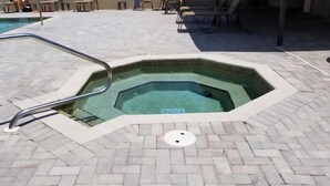 Una bañera de hidromasaje hexagonal con escalera metálica, rodeada por un patio empedrado con sillas y mesas.
