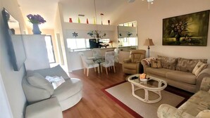 Una sala de estar con sofá, sillones, una mesa de centro y una zona de comedor con sillas y una mesa.