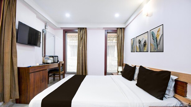 A hotel room with a bed, desk, TV, and artwork on the wall. - Deluxealandur Near Chennai Airport (Dhanbad)