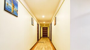 A hotel hallway with a wooden floor, white walls, and framed pictures on the walls. - Deluxealandur Near Chennai Airport (Dhanbad)