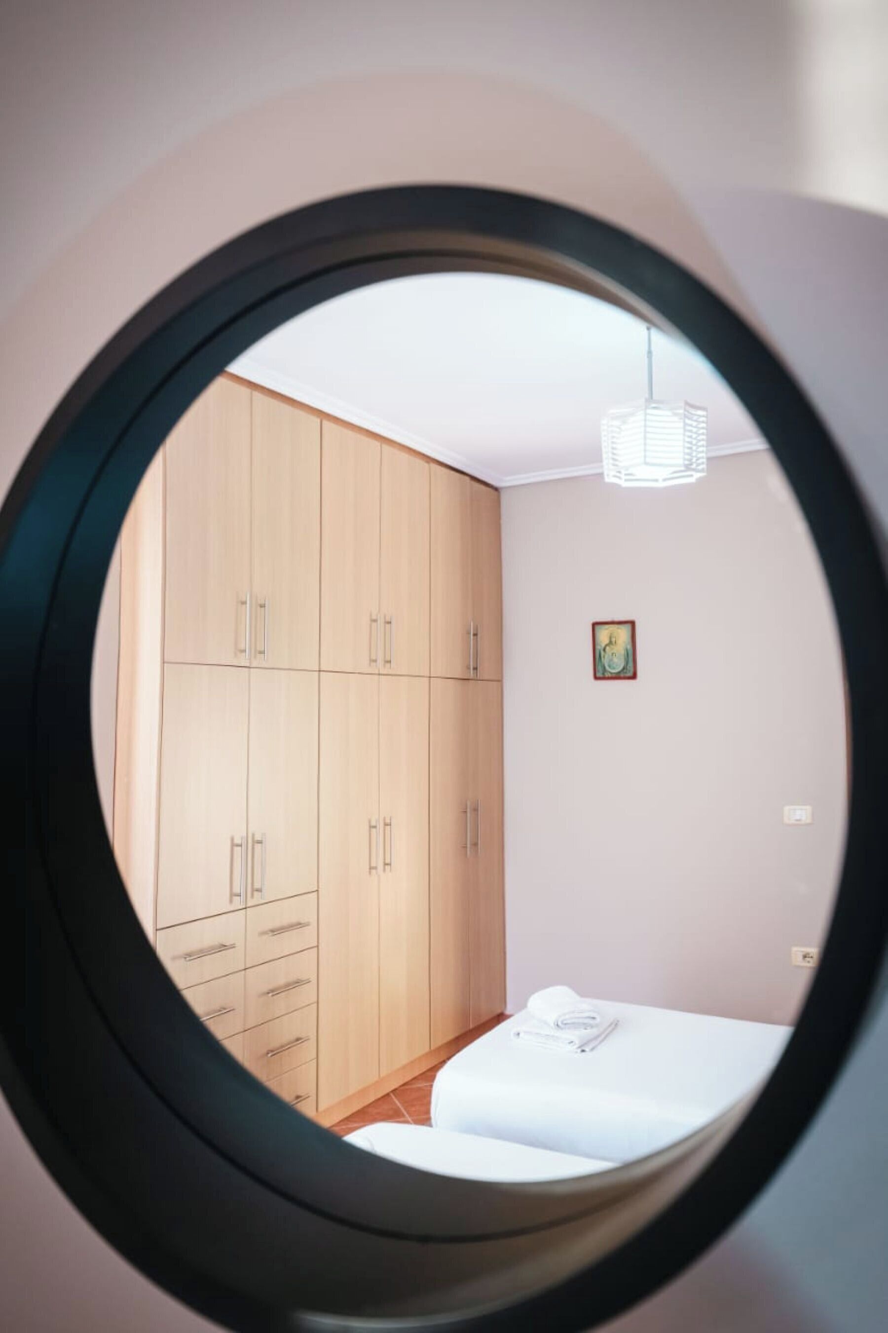 A bedroom with a circular window, wooden wardrobe, and a bed.