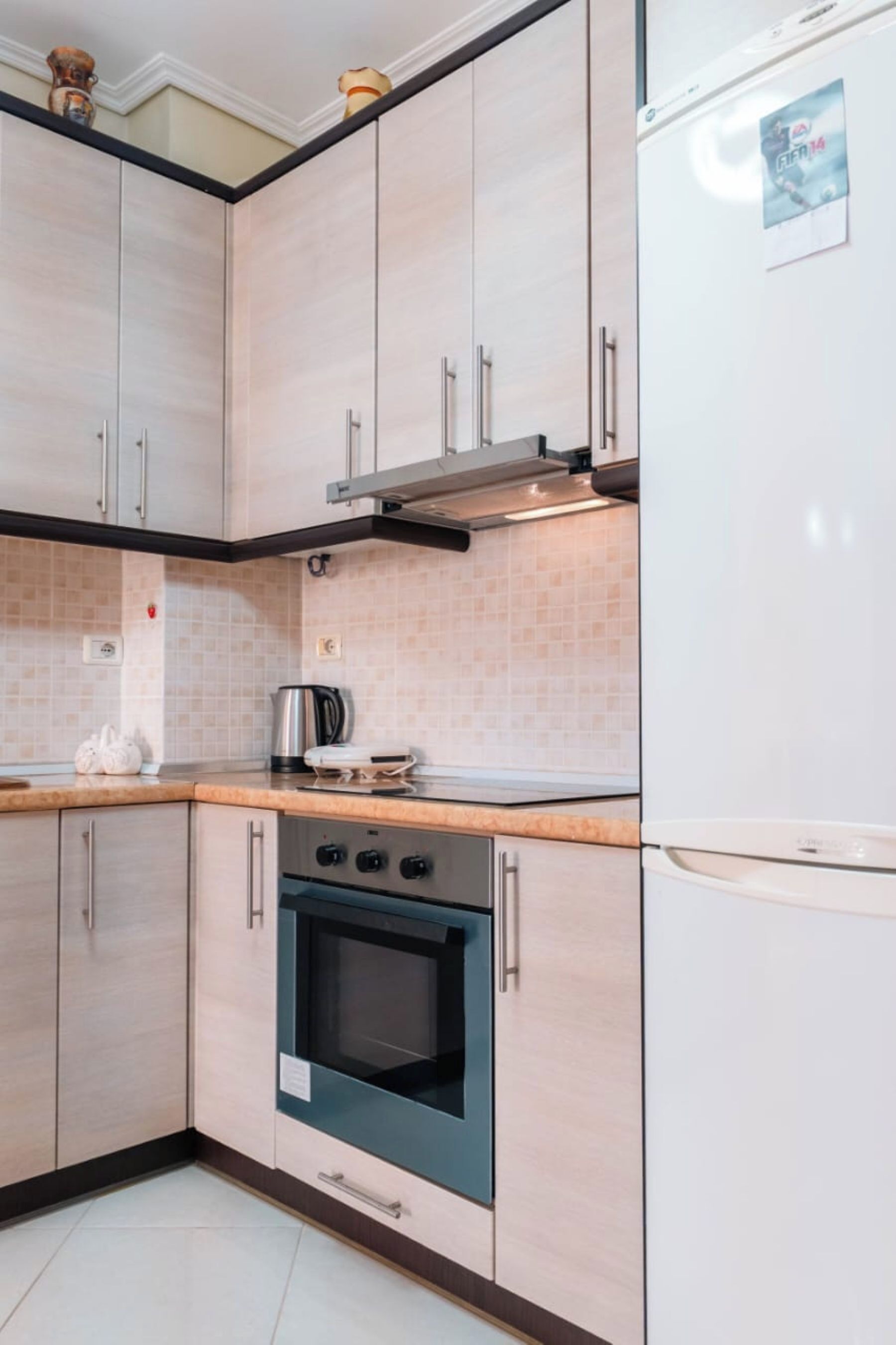 A kitchen with light wood cabinets, a stainless steel range hood, a built-in oven, and a white refrigerator.
