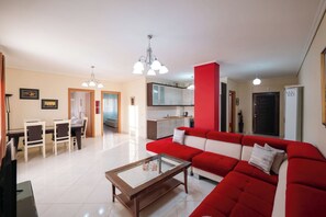 A living room with a red sofa, a glass coffee table, and a dining area with chairs and a table. - Albania Dream Saranda Apartments (Sarandë)