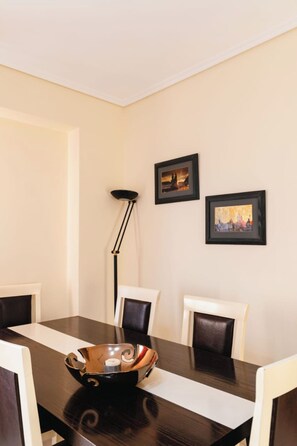 Un comedor con una mesa de madera oscura, sillas blancas, una lámpara de pie negra y dos cuadros en la pared.