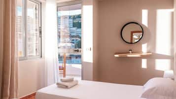 A hotel room with a bed, a window with curtains, a mirror, and a view of buildings.