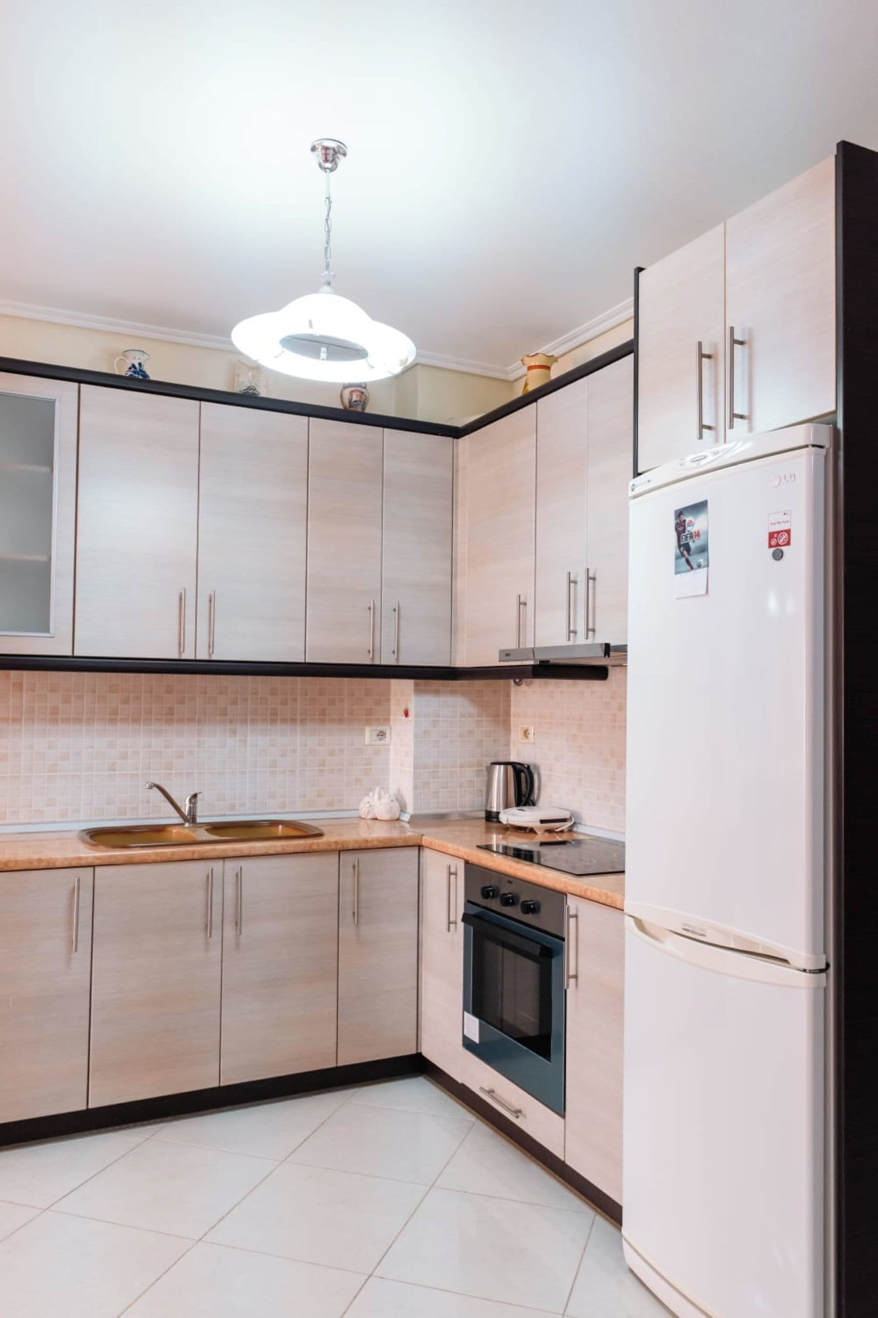 A modern kitchen with light wood cabinets, a stainless steel sink, a built-in oven, and a white refrigerator.