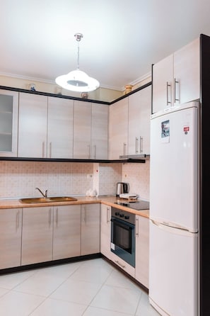 Une cuisine moderne avec des meubles en bois clair, un évier en acier inoxydable, un four encastré et un réfrigérateur blanc.