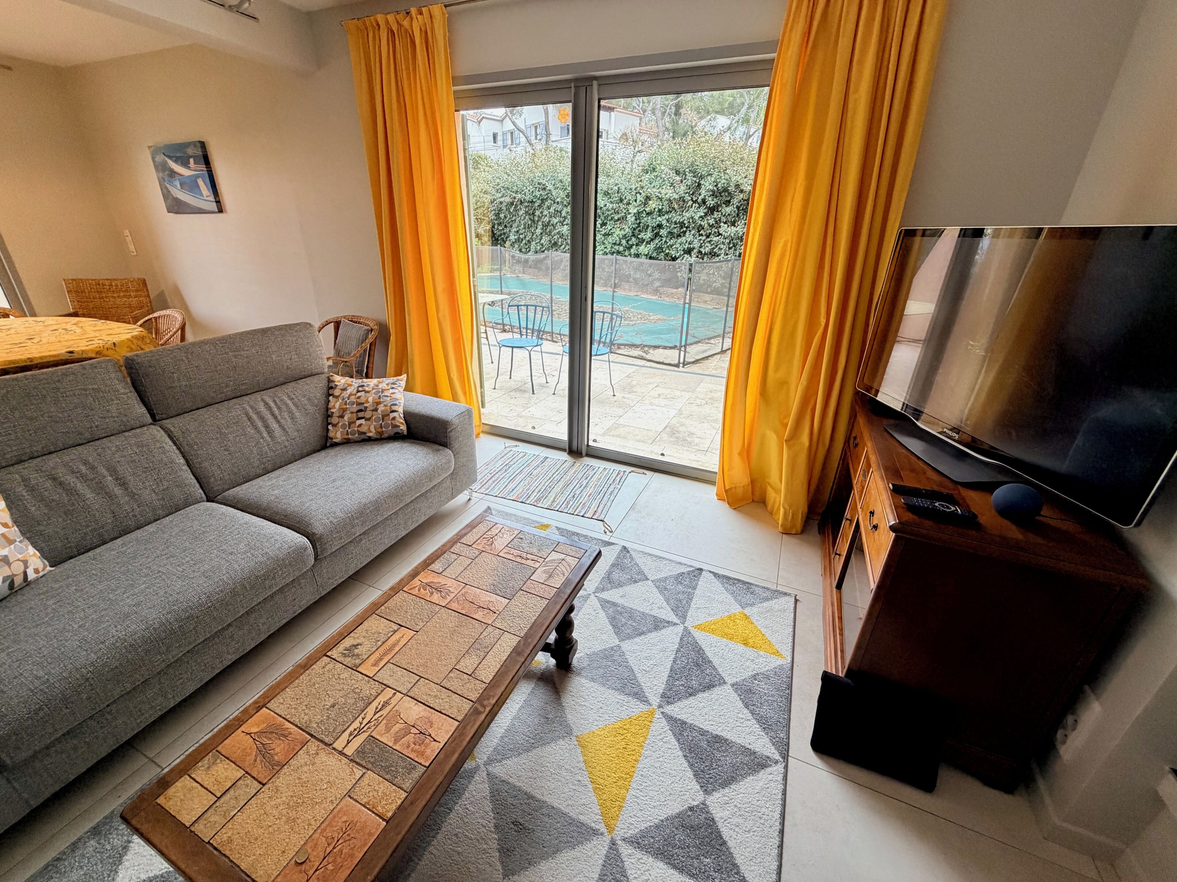 Una sala de estar con sofá, mesa de centro, televisor y cortinas amarillas.