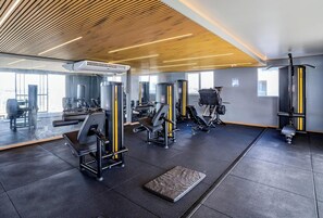 Ein Fitnessraum mit verschiedenen Trainingsgeräten, einem großen Spiegel und einer Holzbalkendecke.