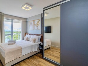 Ein modernes Schlafzimmer mit einem großen Bett, einem Nachttisch, einem Fernseher und einem Balkon mit Blick auf die Stadt.