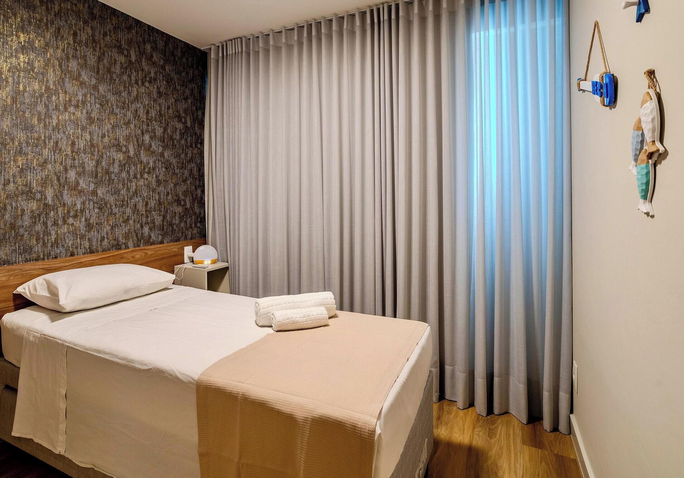 A hotel room with a bed, a nightstand, a lamp, and a wall with a textured pattern.