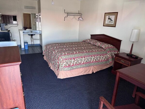 A hotel room with a bed, a desk, a chair, a lamp, and a picture on the wall.