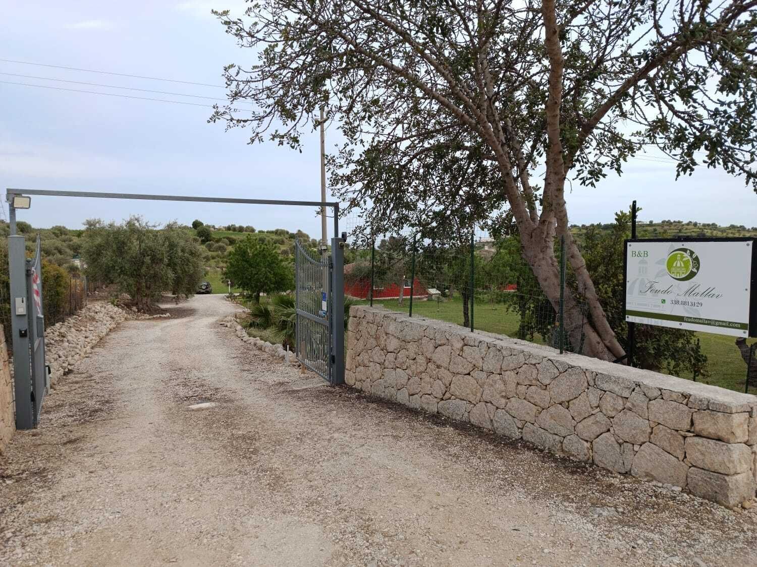 Ein Kiesweg führt zu einem verschlossenen Eingang mit einer Steinmauer und einem Hinweisschild.