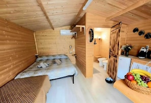 Eine Holzhütte mit einem Bett, einem kleinen Badezimmer und einer Obstschale.