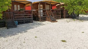A row of wooden cabins with external stairs and a gravel ground. - Feudo Mallav b&b Noto (Avola)
