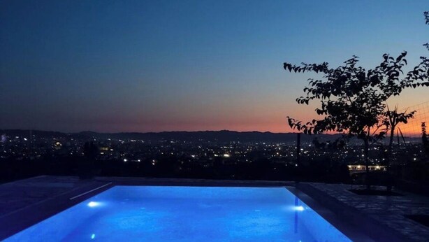 A rectangular pool with blue lighting, surrounded by a cityscape at dusk.