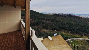 A wooden balcony with a view of a hillside and distant buildings.