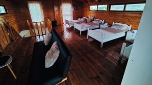 A cabin with wooden walls, a black sofa, three single beds, and a dining table.