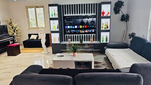 A living room with a black piano, a sofa, a coffee table with a plant, a TV, and a bookshelf with decorative items.