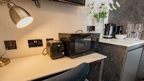 A kitchenette with a microwave, toaster, and coffee maker, a small table with a chair, and a vase with flowers on the counter. - Second Floor Suite | Rathmines | WiFi & Comfort (Dublin)