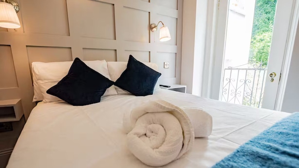A neatly made bed with white linens, two dark pillows, and a rolled towel. - Second Floor Suite | Rathmines | WiFi & Comfort (Dublin)