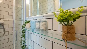 A bathroom with white tiled walls, a glass shower enclosure, a plant in a burlap sack, and a towel rack with a towel and a bag labeled 'FieldDay'. - Second Floor Suite | Rathmines | WiFi & Comfort (Dublin)