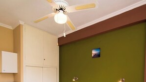 Un letto matrimoniale con poggiatesta in legno, una ventola a soffitto, un comodino piccolo, un'armadio bianco e una parete verde decorativa.