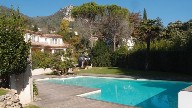 Une piscine dotée d’une terrasse en bois, entourée de verdure et avec une chaîne de montagnes en toile de fond.