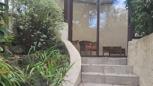 Un escalier extérieur abrité menant à un espace de détente doté d’un toit en verre, le tout entouré de verdure.