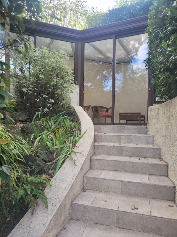 A covered outdoor staircase leading to a seating area with a glass roof, surrounded by greenery.