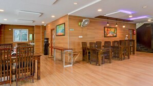 A spacious room with wooden flooring, multiple wooden tables and chairs, ceiling fans, and wall-mounted artwork. - Deluxepurple Square (Hyderabad)