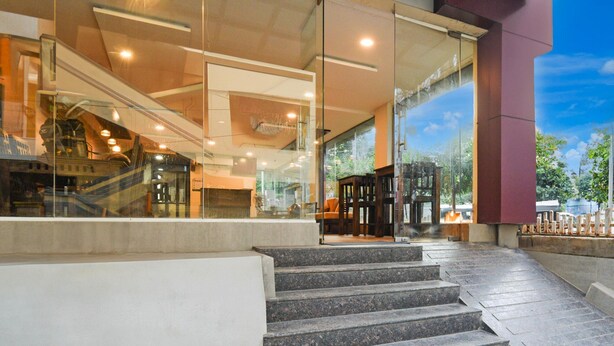 A modern building entrance with a staircase leading to a glass door, a visible elevator, and a clear view of the outdoors. - Deluxepurple Square (Hyderabad)