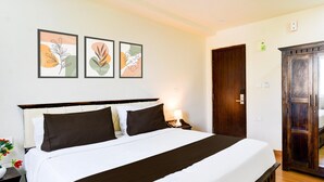 A neatly made bed with a dark headboard, a bedside table with a lamp, and three framed artworks on the wall. - Deluxepurple Square (Hyderabad)