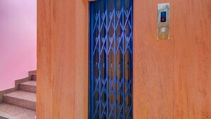 A staircase leading to a blue metal gate, a wall-mounted elevator control panel, and a pink wall. - Deluxeshanthaa Residency (Hyderabad)