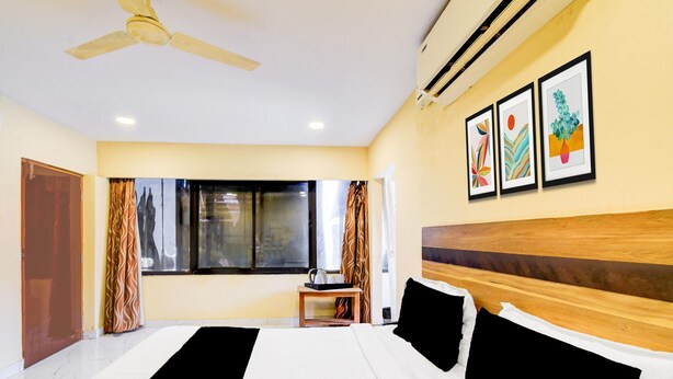 A hotel room with a bed, ceiling fan, artwork on the wall, and a window with curtains. - Deluxeshanthaa Residency (Hyderabad)
