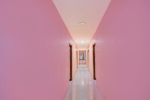 Un long couloir étroit aux murs roses et au sol brillant, qui mène à une porte au fond.