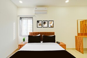 A hotel room with a bed, bedside tables, a window, an air conditioner, and wall art. - Deluxe Suchitra Kompally Sun Moon Hotels (Hyderabad)