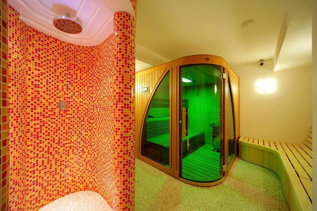 A room with a mosaic-tiled wall, a wooden bench, and a glass door leading to a green-lit space.