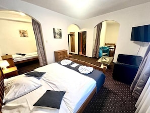 Habitación de hotel con cama, escritorio, silla, televisor y baño visible a través de un arco.