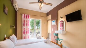 Habitación de hotel con dos camas, ventilador de techo, televisor, ventana con cortinas y un escritorio pequeño con espejo.