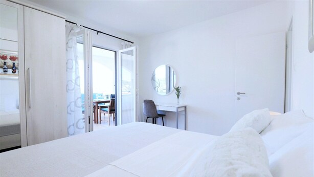 Een hotelkamer met een bed, een bureau, een stoel, een spiegel en uitzicht door een open deur.