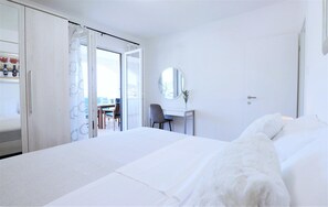 Een hotelkamer met een bed, een bureau, een stoel, een spiegel en uitzicht door een open deur.