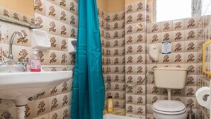 Kylpyhuone, jossa on pesuallas, wc, suihkuverho ja laatoitetut seinät.