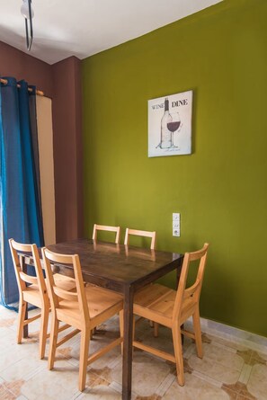 Ein Essbereich mit Holztisch und Stühlen, einer grünen Wand und einem Poster einer Weinflasche.