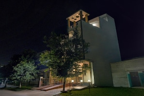 Un edifici modern amb una torre, una entrada tancada amb reixa i un camí ben il·luminat.