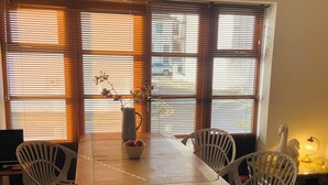 A dining area with a wooden table, four chairs, a vase with flowers, and a window with blinds. - Central Hove near beach & lawns (Brighton and Hove)