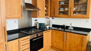 A kitchen with wooden cabinets, a stainless steel range hood, a Bosch oven, a black countertop, and a sink. - Central Hove near beach & lawns (Brighton and Hove)