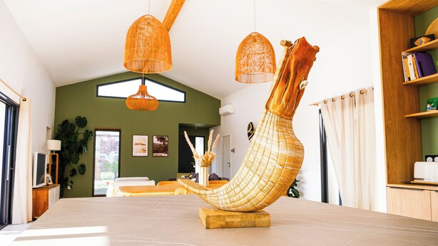 Un intérieur moderne agrémenté d’une sculpture tissée originale posée sur une table en marbre, d’étagères en bois et d’un mur vert.