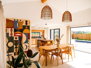 A modern kitchen with wooden cabinets, a dining area with a wooden table and chairs, and a large window. - Villa NOOSA - Saltwater pool - Terrace - Seignosse (Seignosse)