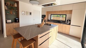 Une cuisine moderne dotée d’un îlot en marbre, de meubles en bois, d’un four encastré et d’une grande fenêtre.